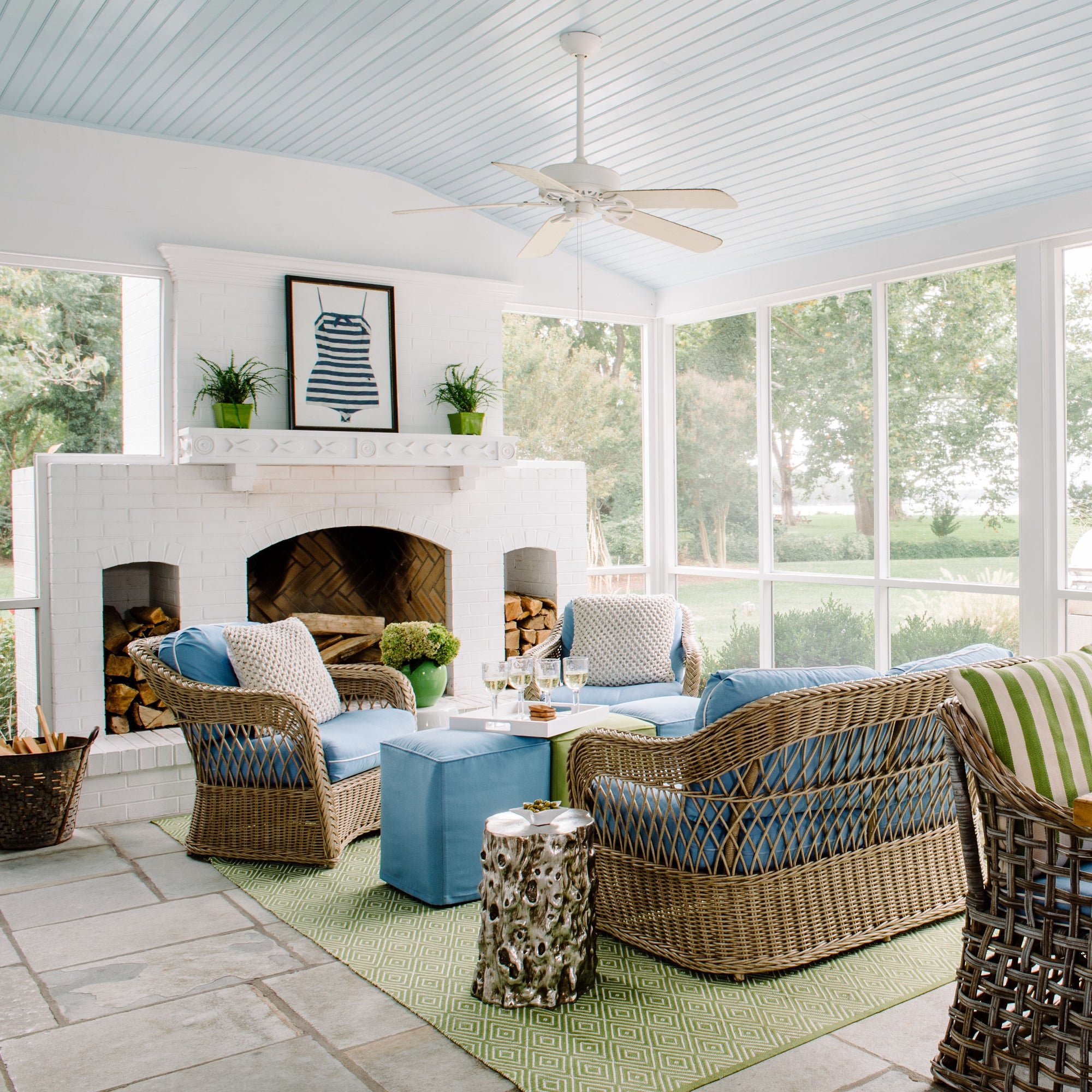 Large porch with white fireplace, soft blue ceiling and wicker furniture with green and blue accents. Interior design by Jamie Merida.